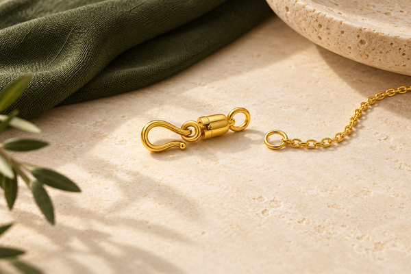 Illustrative gold-coloured amulet connector and fine chain on cream stone beside olive fabric