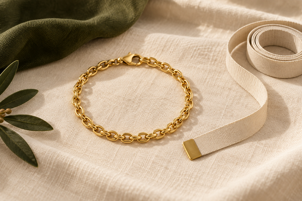 Illustrative gold chain bracelet beside a measuring tape on cream linen with dark olive fabric