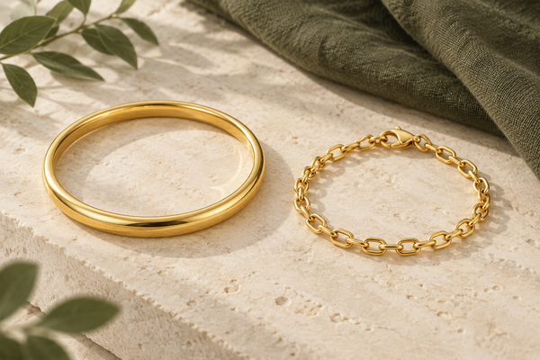 Illustration of a circular gold bangle beside a flexible gold link bracelet on cream stone