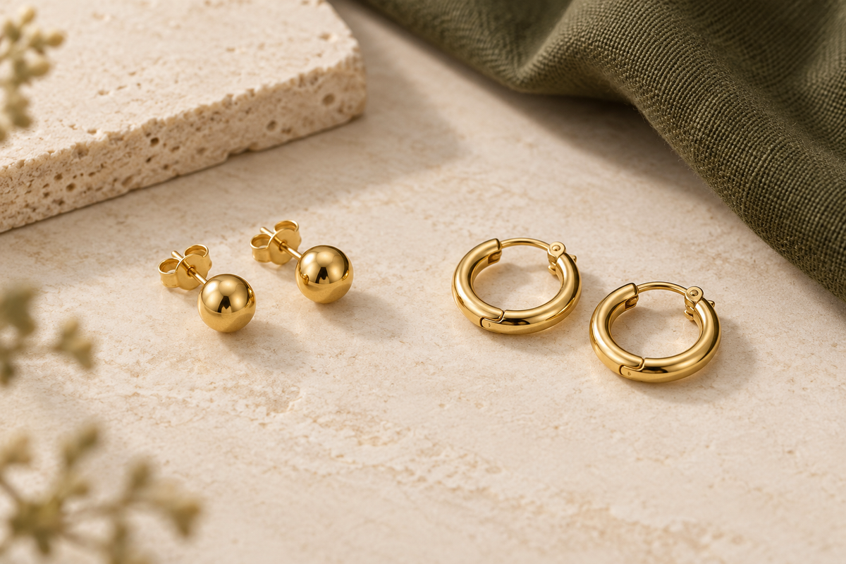 Illustration of plain gold stud earrings with butterfly backs beside small hinged gold hoop earrings on cream stone