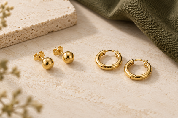Illustration of plain gold stud earrings with butterfly backs beside small hinged gold hoop earrings on cream stone