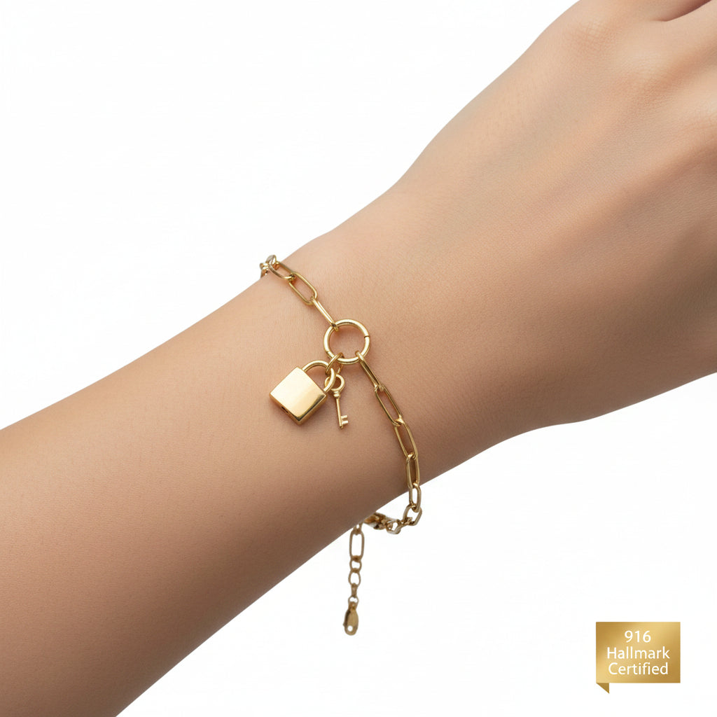 Close-up of lock and key charms on a 916 Gold Paperclip bracelet.