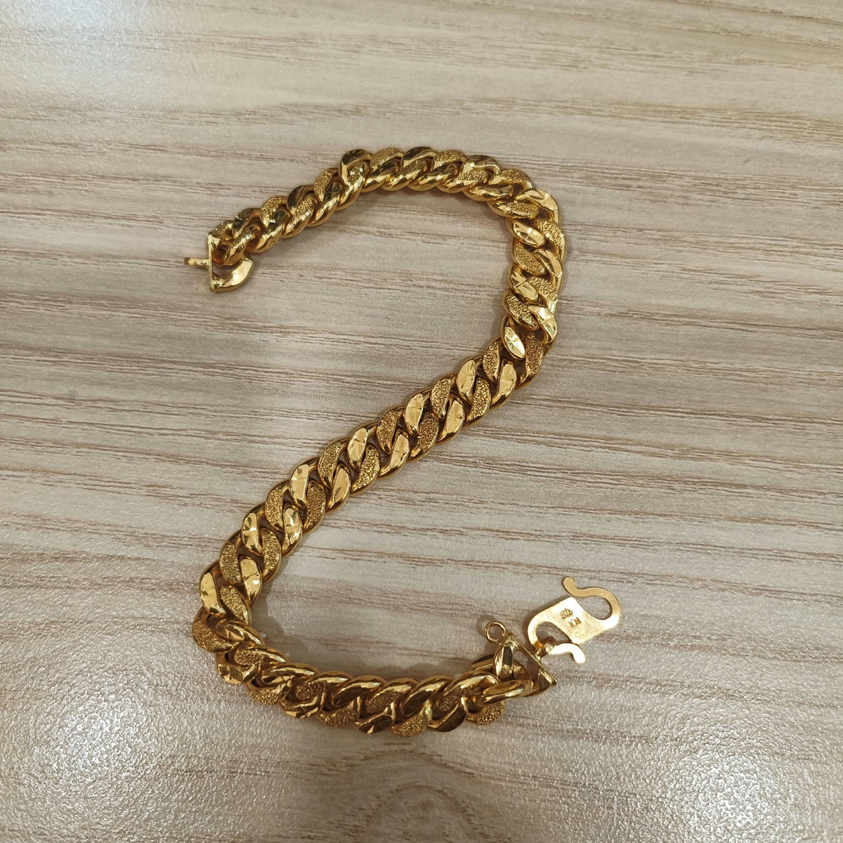Cowboy-link gold bracelet laid in a curve on a wood-grain surface