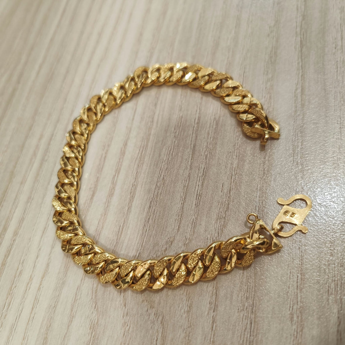 Cowboy-link gold bracelet arranged in a circle on a wood-grain surface