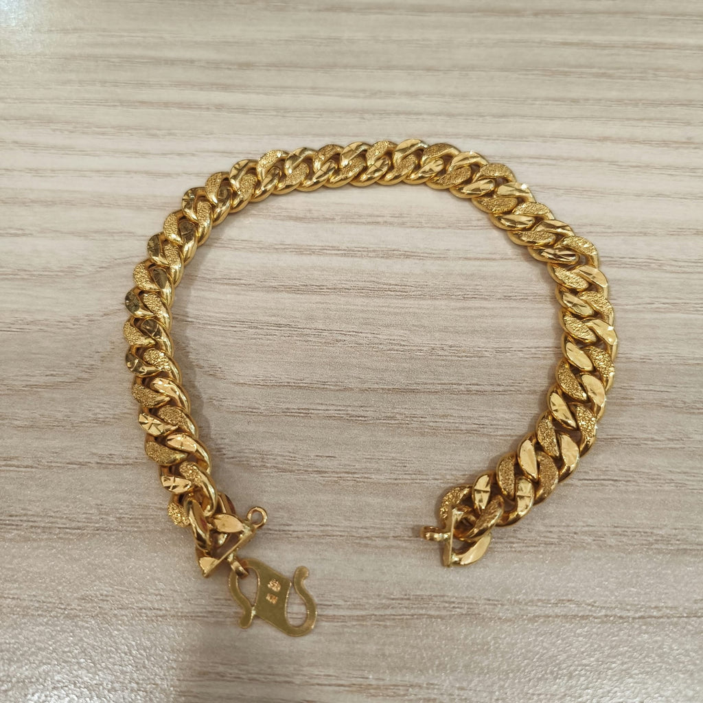 Cowboy-link gold bracelet arranged with open ends on a wood-grain surface