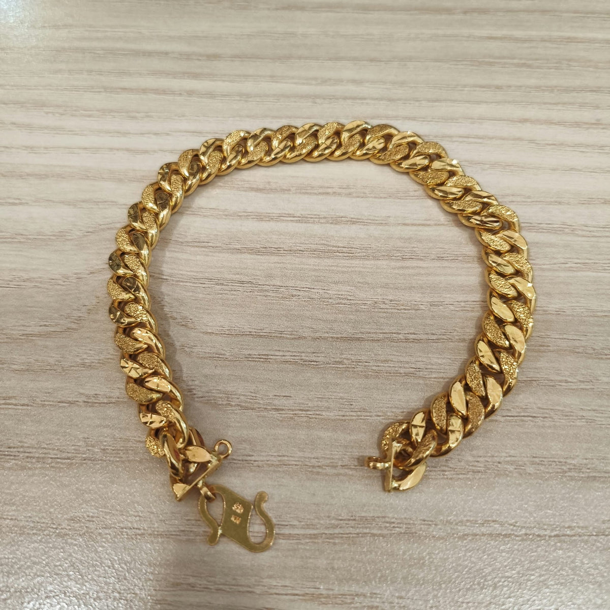 Cowboy-link gold bracelet arranged with open ends on a wood-grain surface