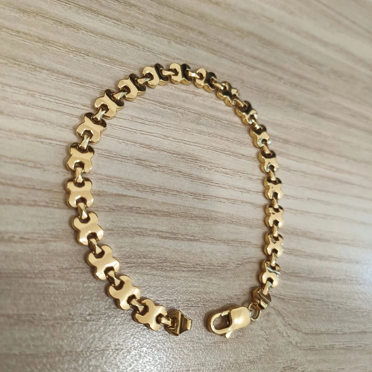 Close-up of the 22K / 916 gold geometric-link bracelet and lobster clasp on a wood surface