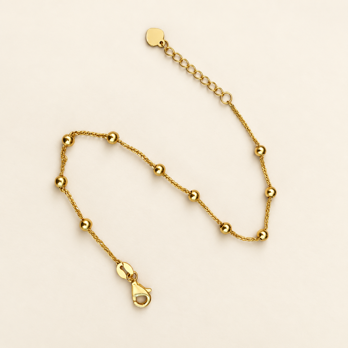 Curved view of the 916 gold bead bracelet showing its fine chain, lobster clasp and heart-shaped end tag