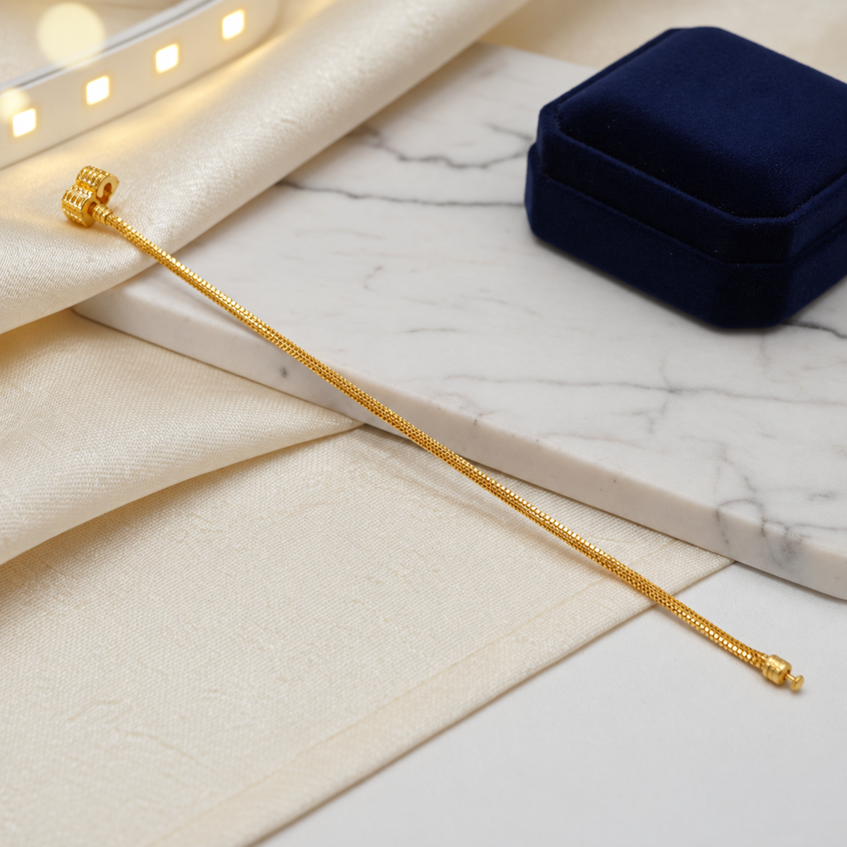 Guild Bullion 22K / 916 gold Charm-Cut Bracelet extended diagonally on satin and marble beside a navy jewellery box