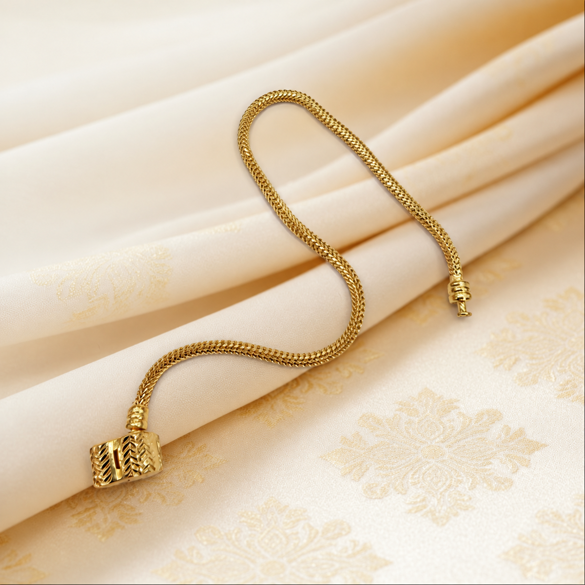 Guild Bullion 22K / 916 gold Charm-Cut Bracelet showing fine chain texture and decorative barrel clasp on patterned satin