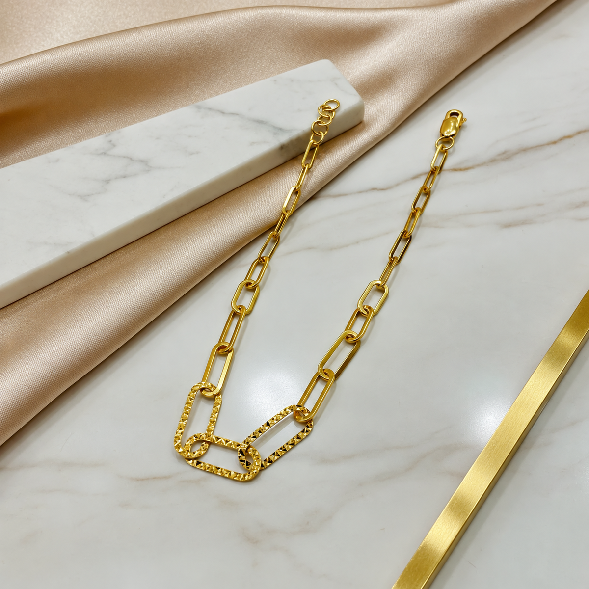 BR21200 916 gold Clip Bracelet V3 arranged on marble, showing faceted centre links, lobster clasp and extension rings