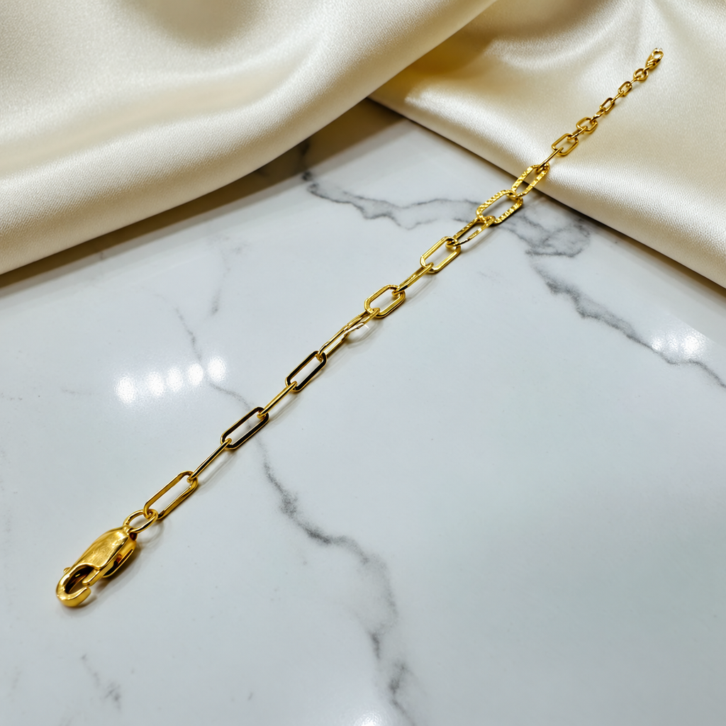 Full extended view of the 916 gold Clip Bracelet V3 with elongated smooth links and faceted centre links on marble