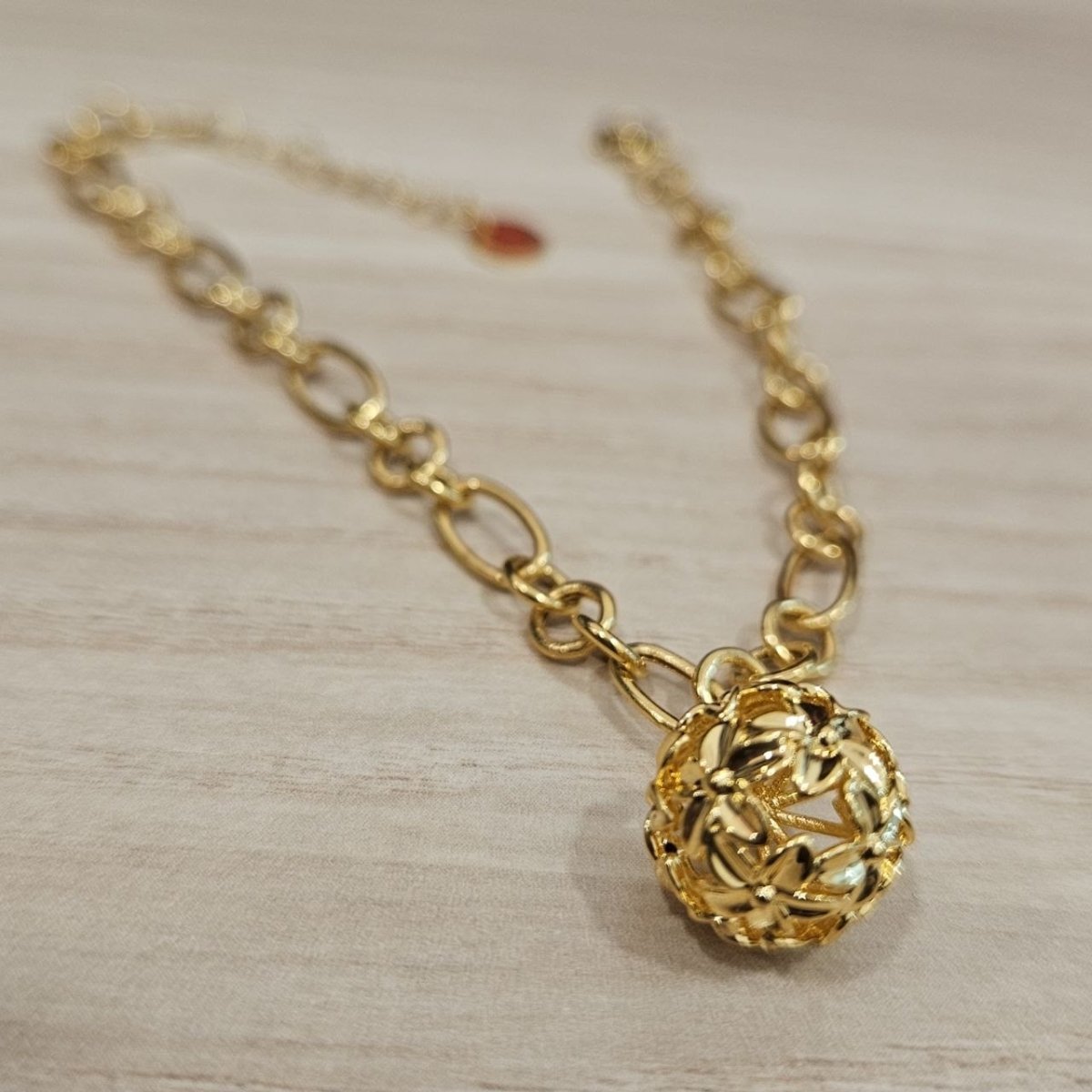 Angled close-up of the openwork flower-ball charm and oval and round links