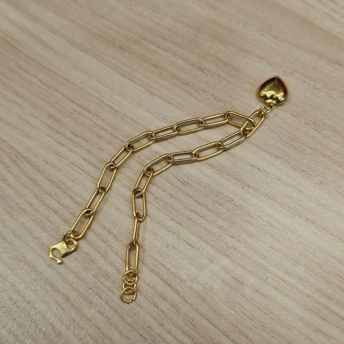 916 gold Dangling Heart Bracelet V2 BR25203 folded on wood with elongated links and polished heart charm