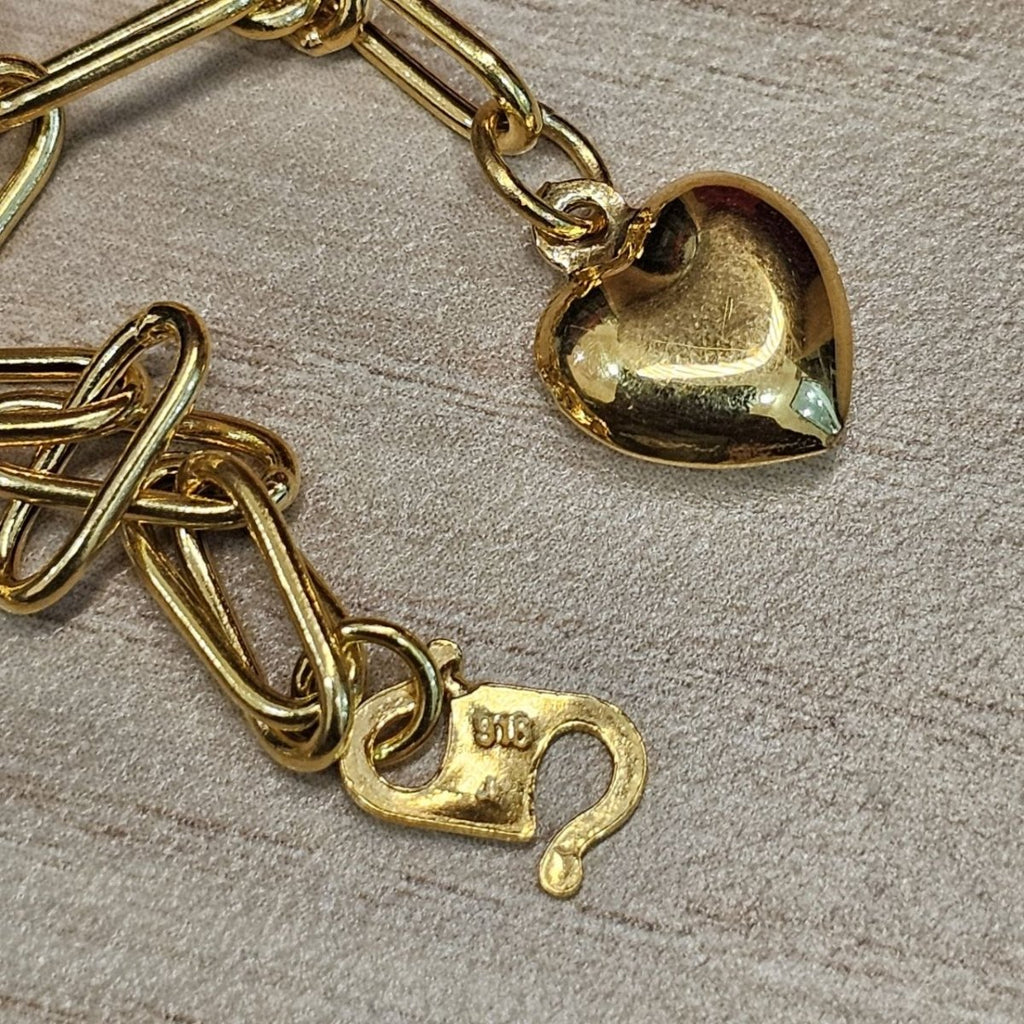 Close-up of polished heart charm, elongated links and hook clasp on 916 gold bracelet BR25205