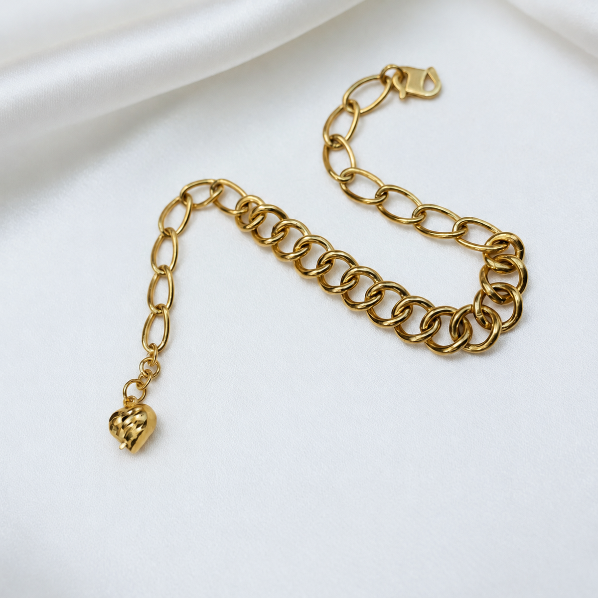916 gold dual design link bracelet with faceted heart charm and hook clasp curved on white satin
