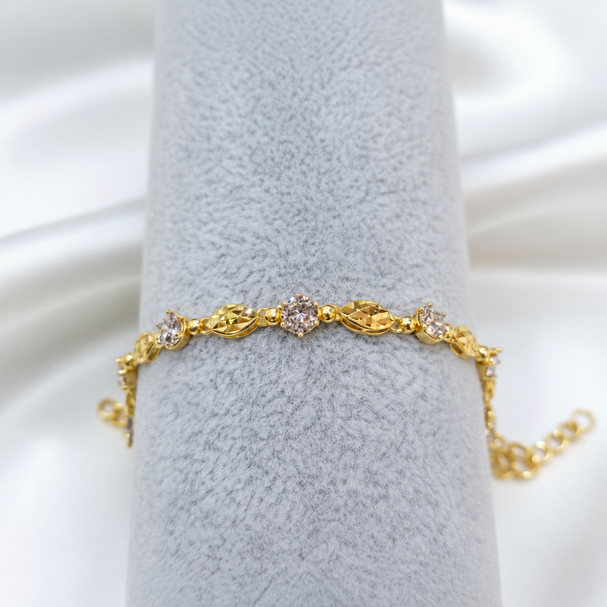 Guild Bullion BR7036 916 gold bracelet showing faceted oval links and round silver-coloured accents on grey velvet