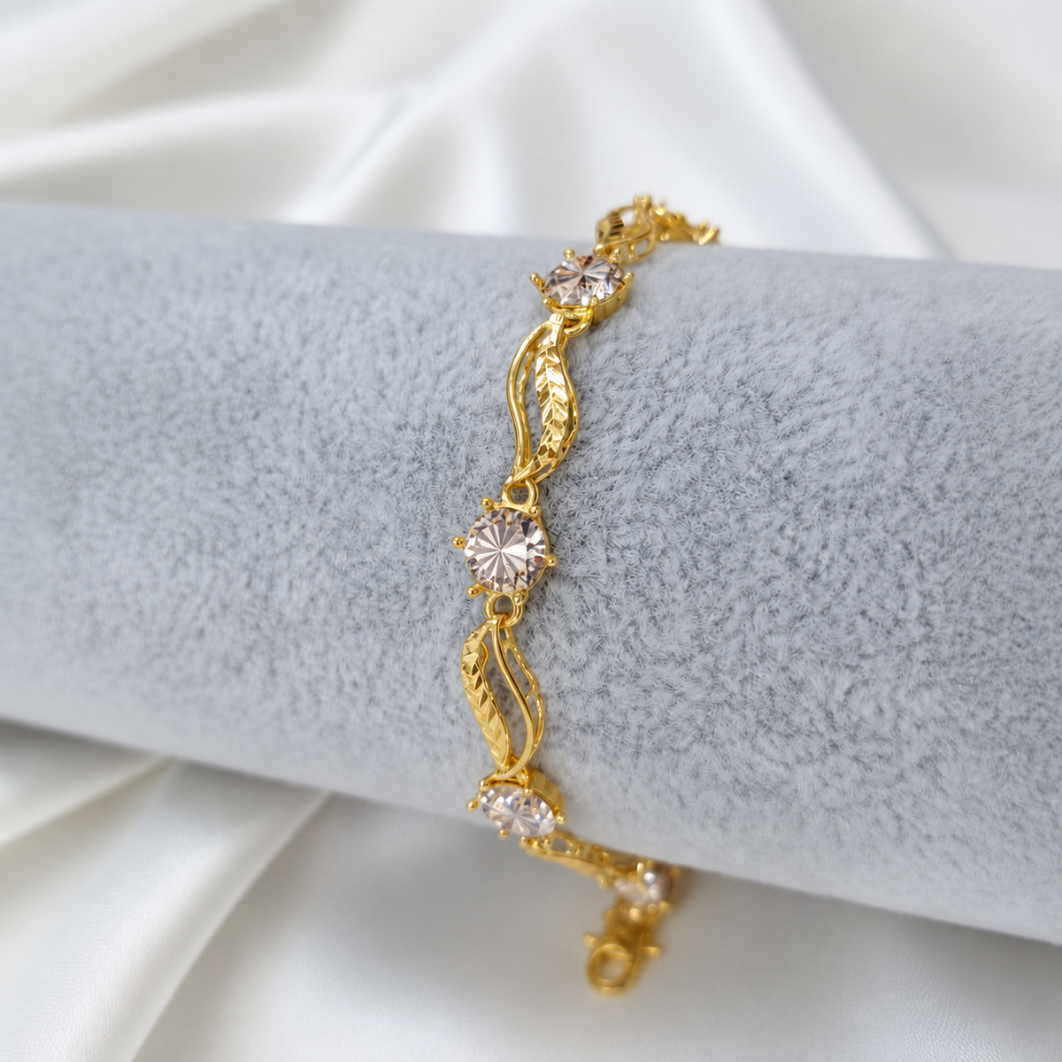 Reference leaf-link bracelet close-up on grey velvet showing faceted gold links and round silver-coloured accents