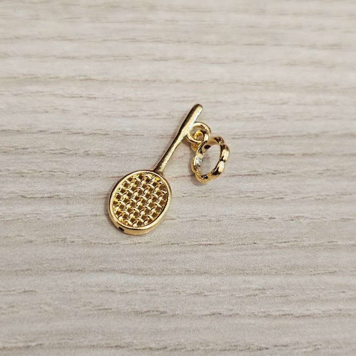 Guild Bullion 916 gold badminton racket charm; collection design reference. Check selector for current options and availability.