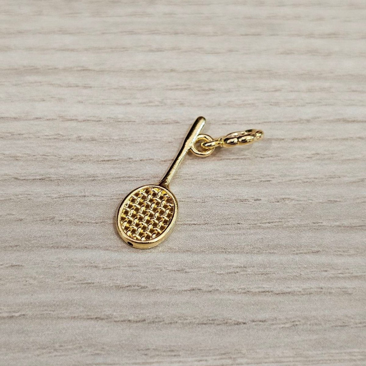 Guild Bullion 916 gold racket charm; collection design reference. Check selector for current options and availability.