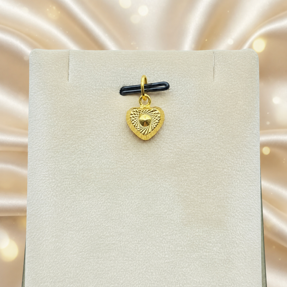 Reference view of a patterned 916 gold heart pendant on a cream jewellery display