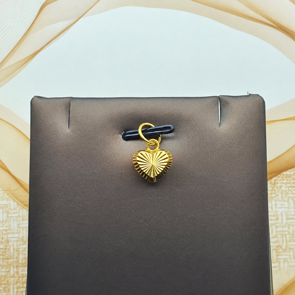 Reference view of a radiating-cut gold heart pendant on a grey display against a geometric background