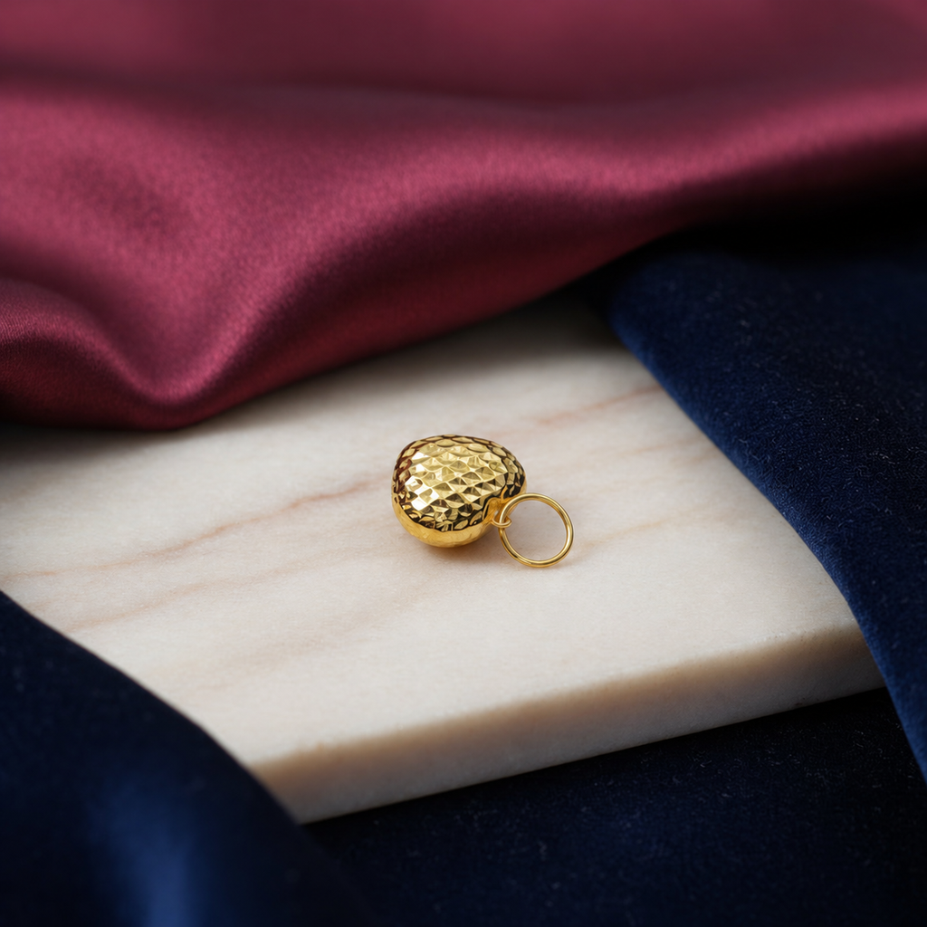 Side view of a yellow-gold 916 faceted heart pendant beside burgundy and navy fabric