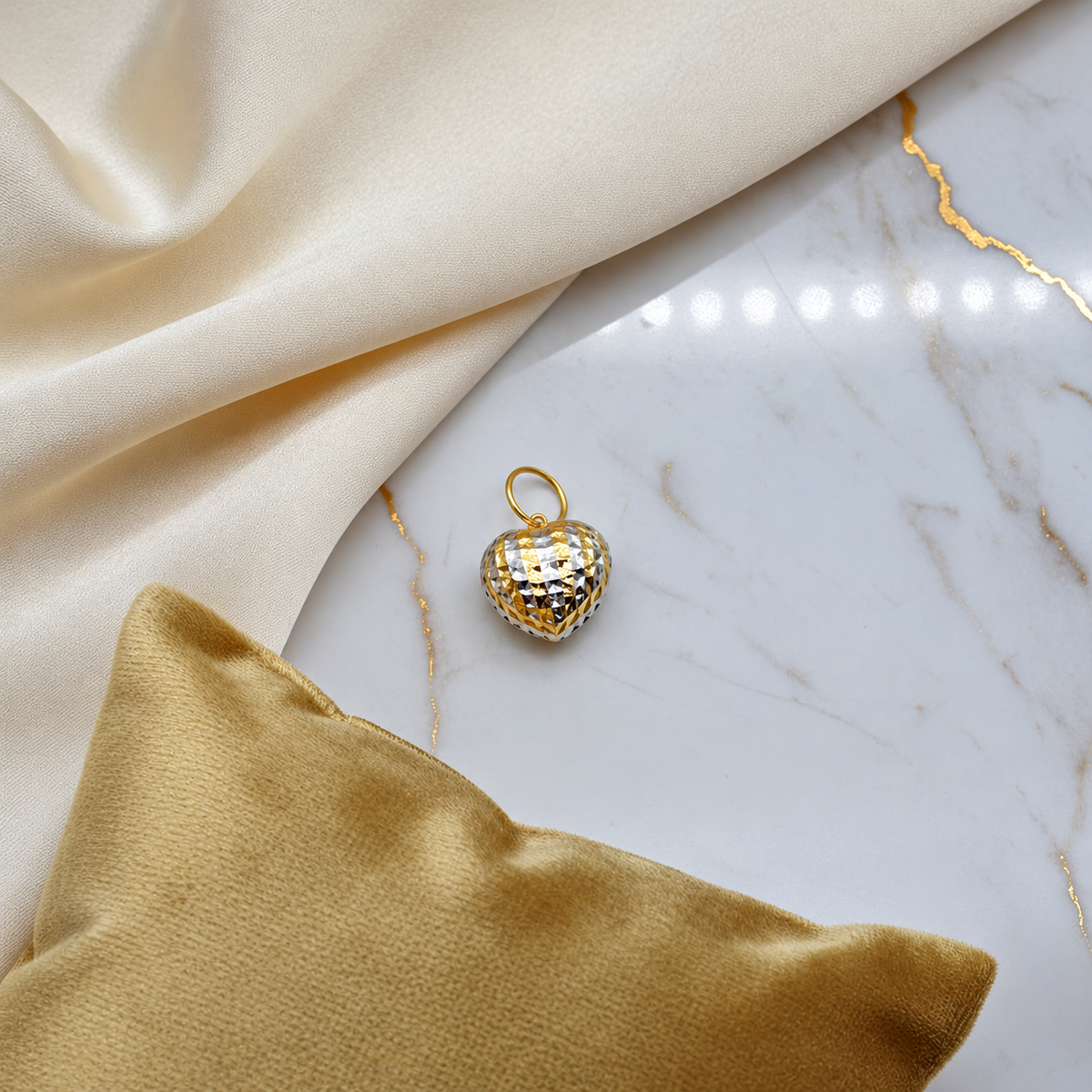 Two-tone 916 heart pendant on pale marble beside cream fabric and a gold cushion