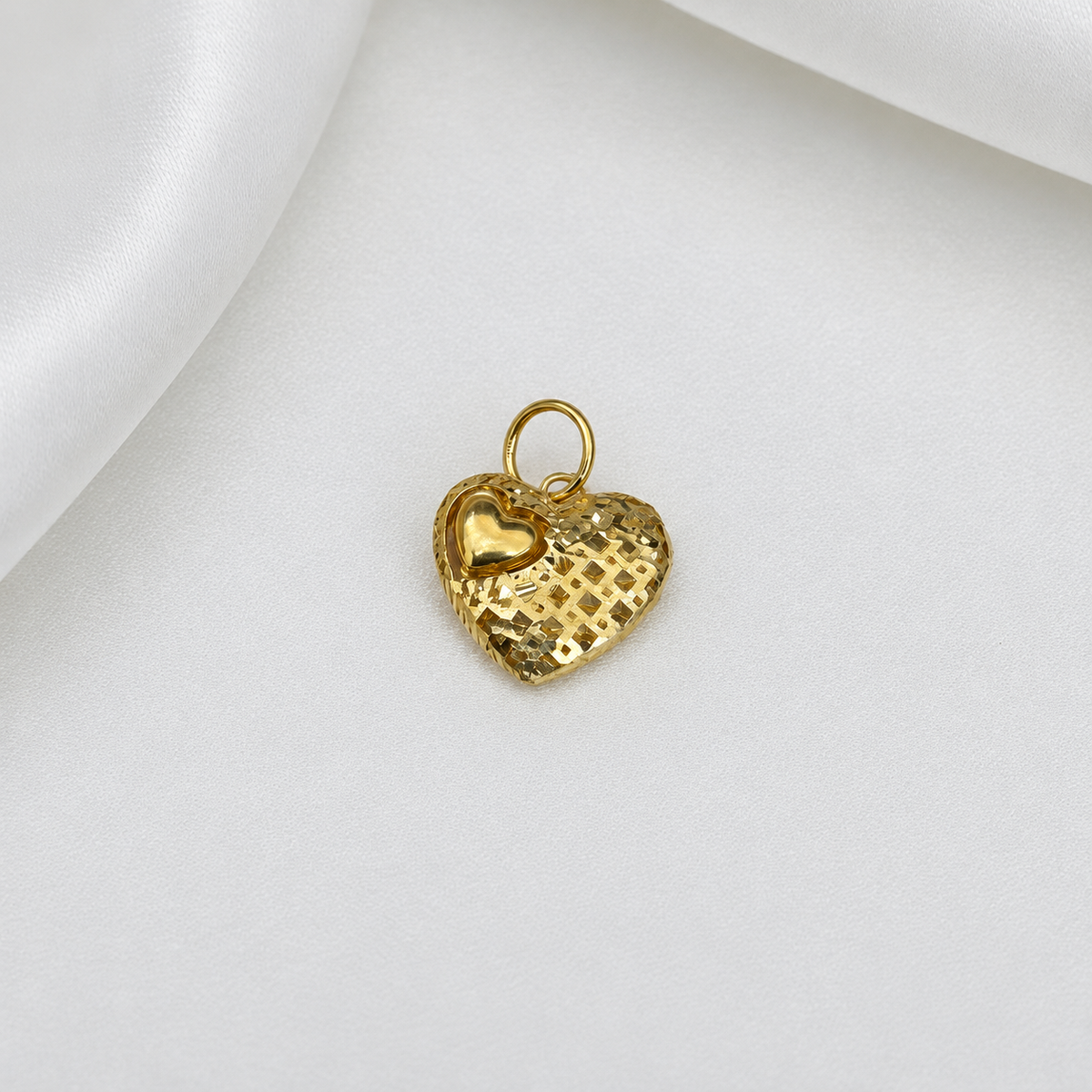 916 gold grid-textured heart pendant with a polished mini-heart accent and gold loop on white satin