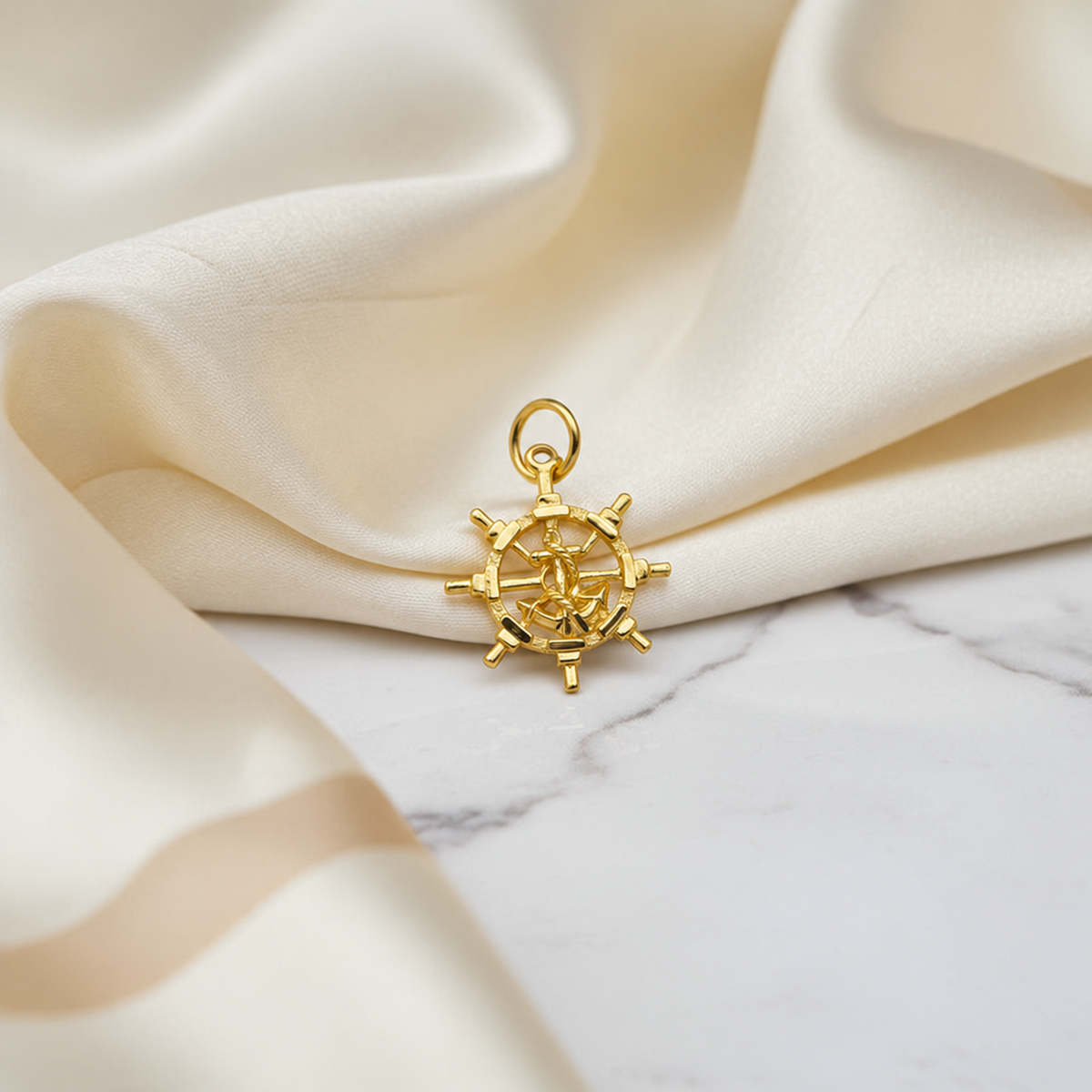 916 gold anchor and openwork ship’s-wheel pendant on marble beside ivory satin