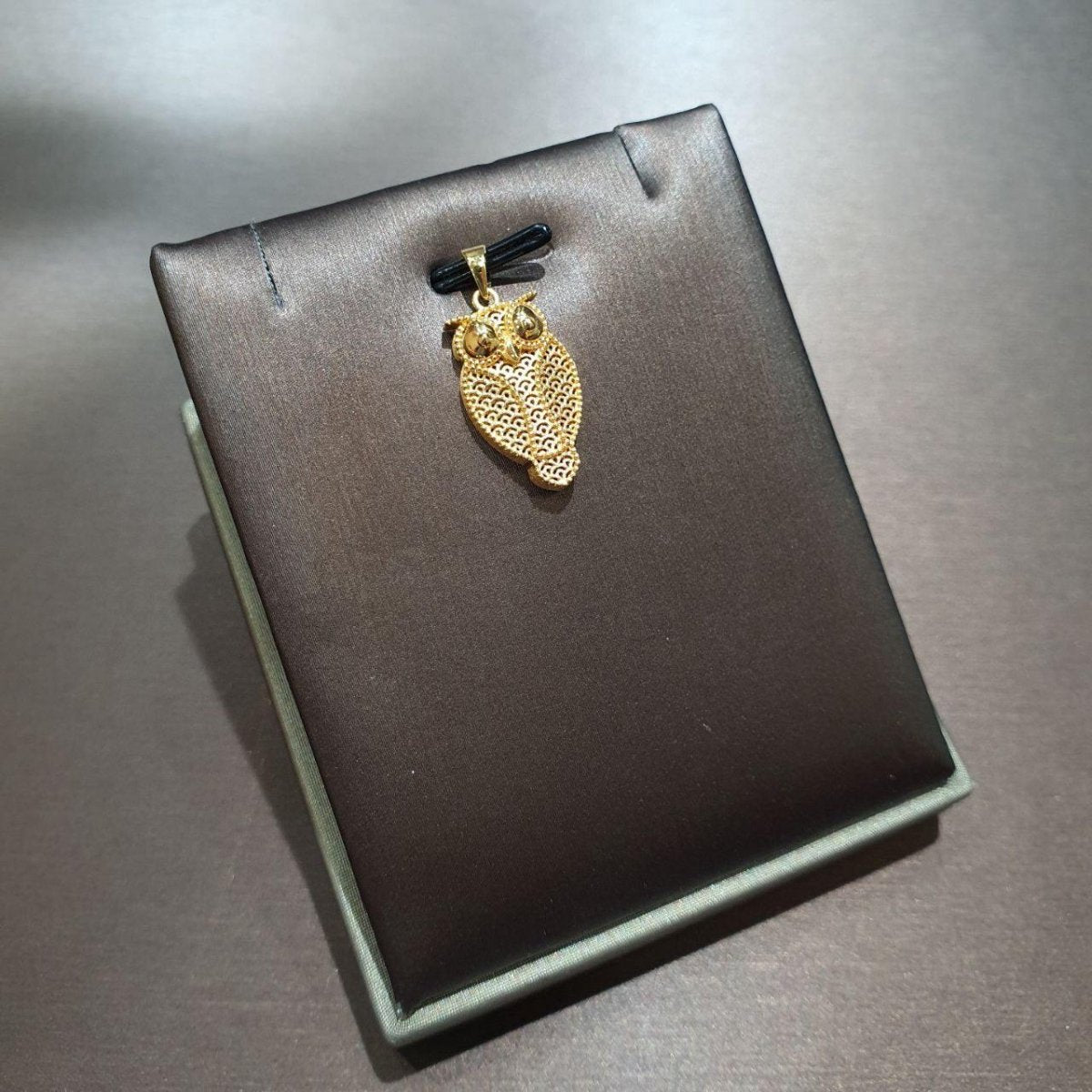 916 gold owl pendant with openwork feather pattern and polished eye details on a grey display