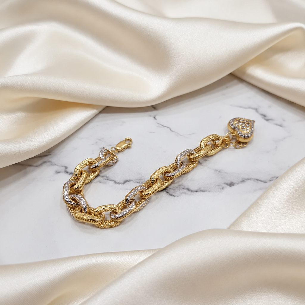 Two-tone 916 gold Regal Link Bracelet with heart charm arranged on white marble beside ivory satin