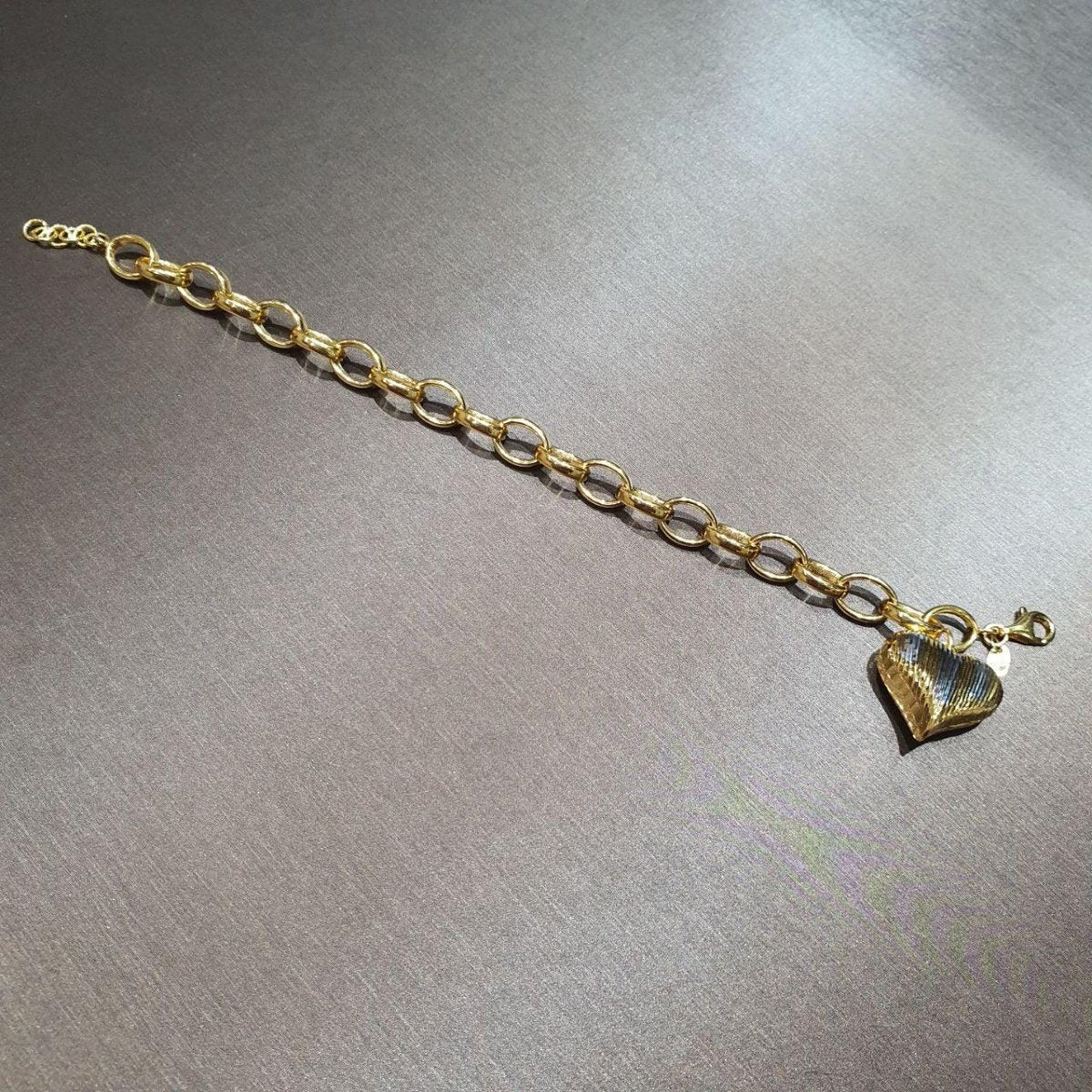 916 gold ring-link bracelet extended on a grey surface, showing a ridged heart pendant, lobster clasp and extension rings