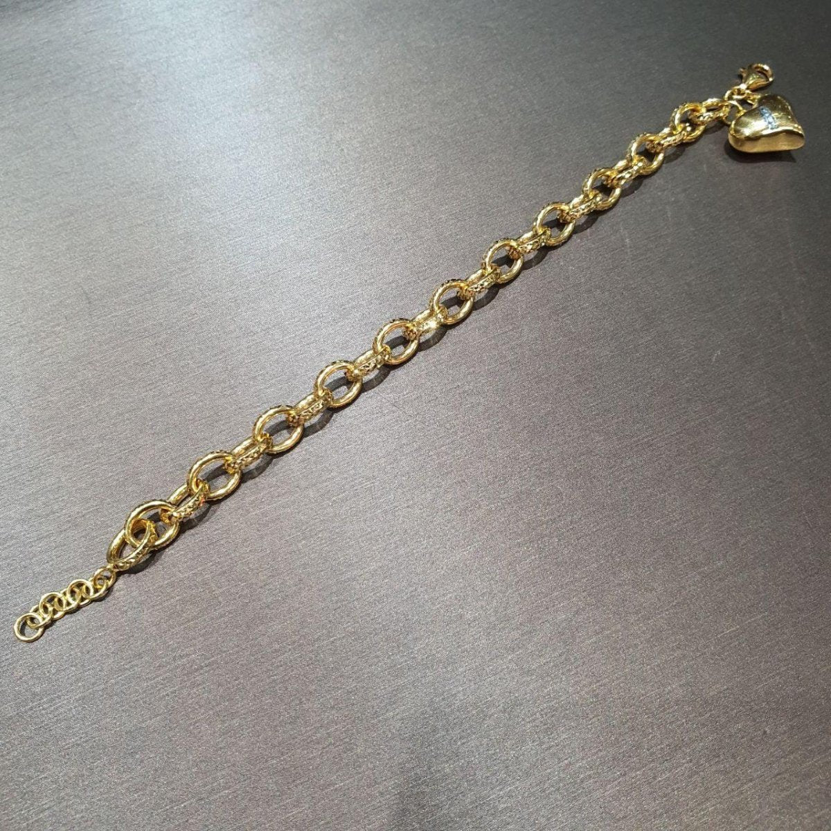 Reverse view of the 22K gold ring-link heart bracelet extended diagonally on a grey surface