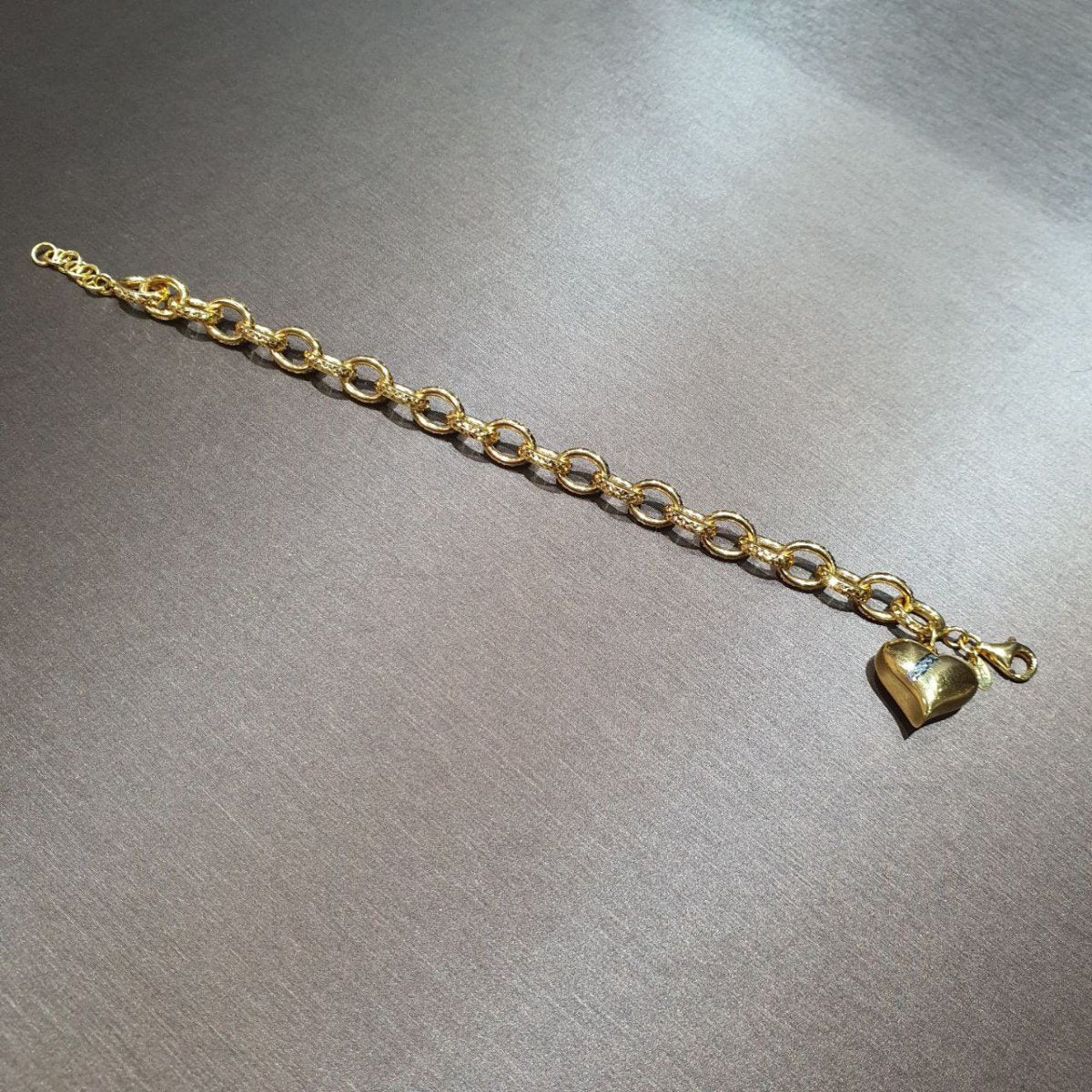 916 gold ring-link bracelet extended on a grey surface with a polished heart pendant and extension rings