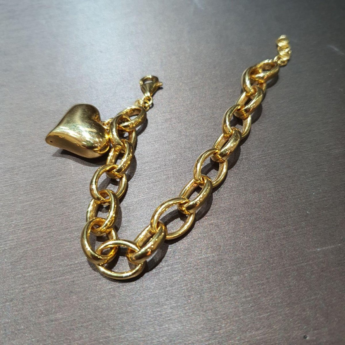 BR19949 916 gold ring-link bracelet with polished heart pendant and larger oval links on a grey surface