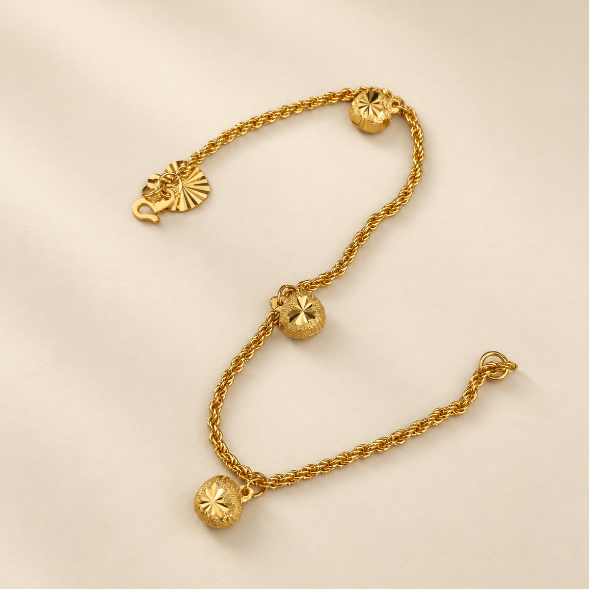 Curved arrangement of the 916 gold hollow rope bracelet showing starburst facets on three textured charms