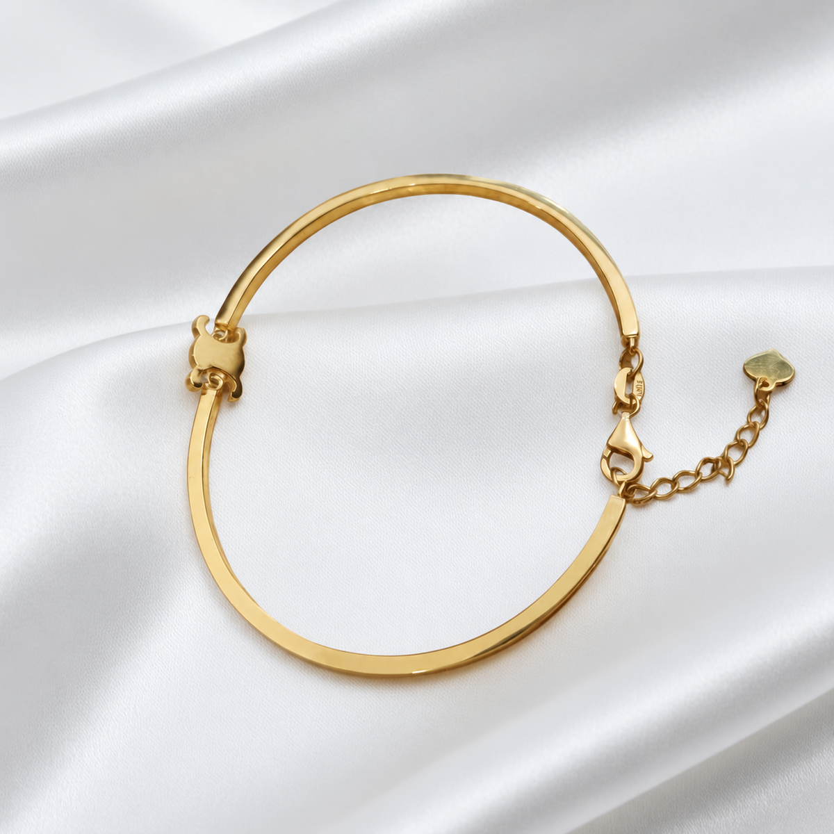 Angled view of the 22K gold Scroll Motif Bangle on satin showing the band and adjustable fastening