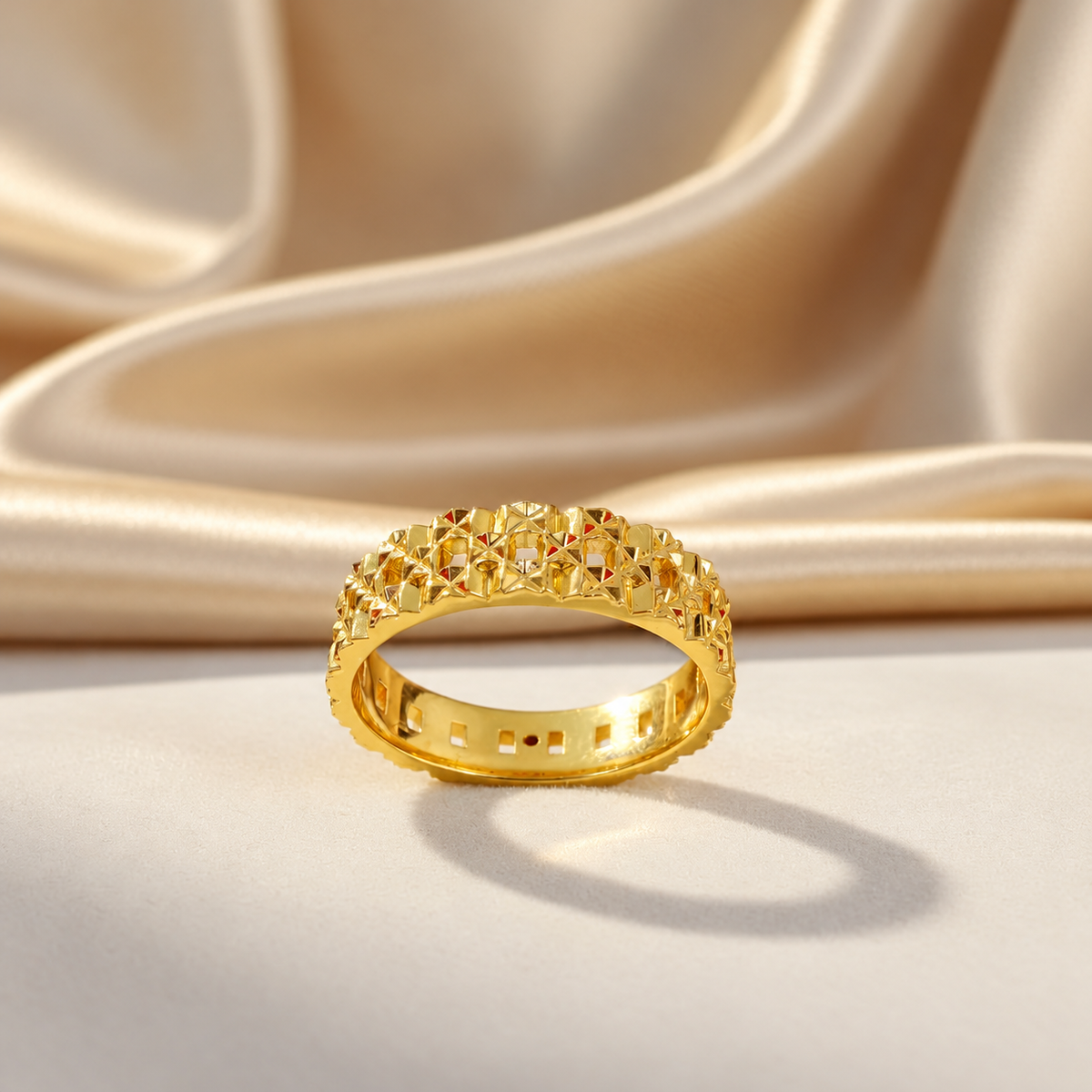 Front view of the 916 gold Slim Keeper ring showing faceted openwork and polished inner band on cream satin