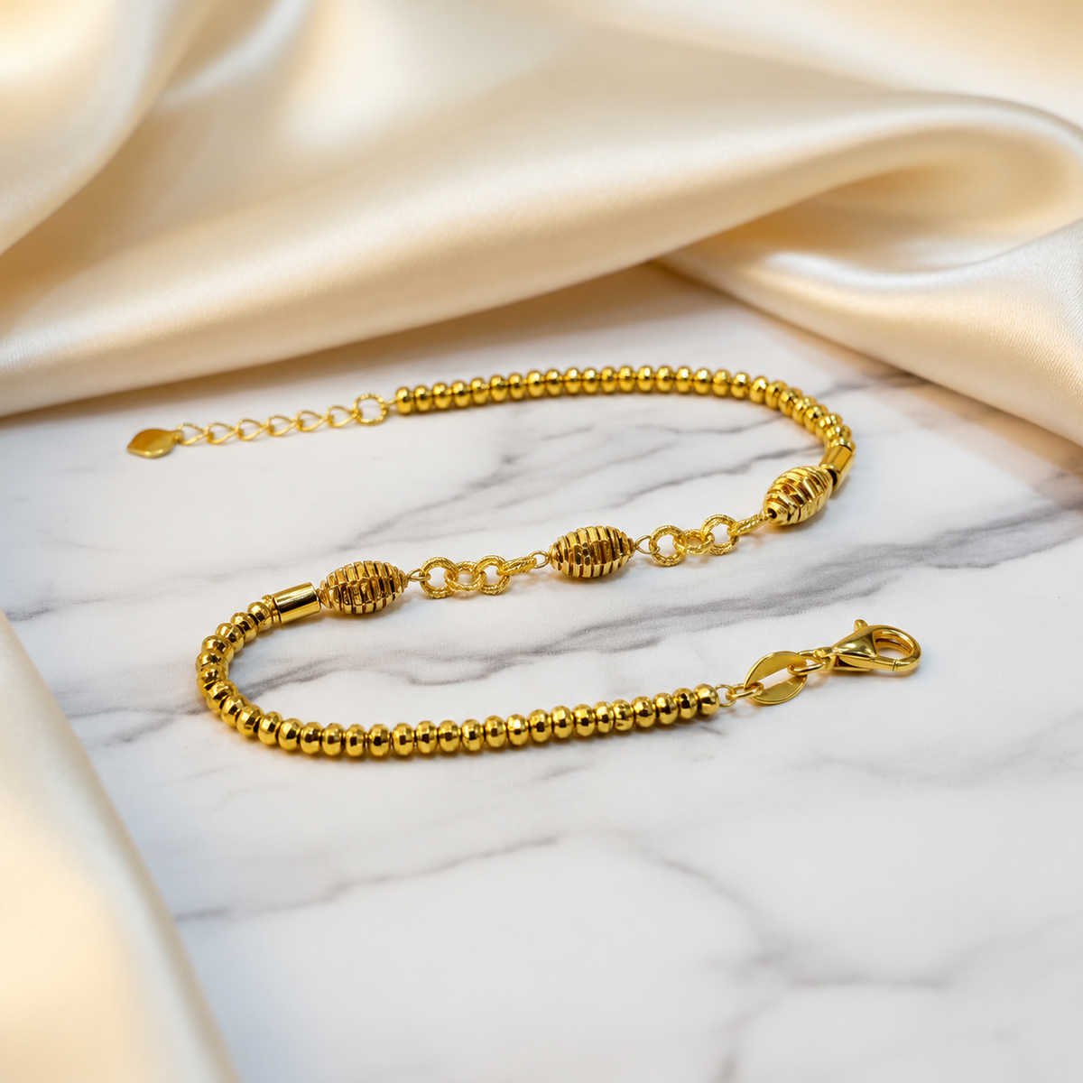 Guild Bullion 22K / 916 gold triple oval bracelet on marble with cream satin, showing all three ribbed oval beads and clasp