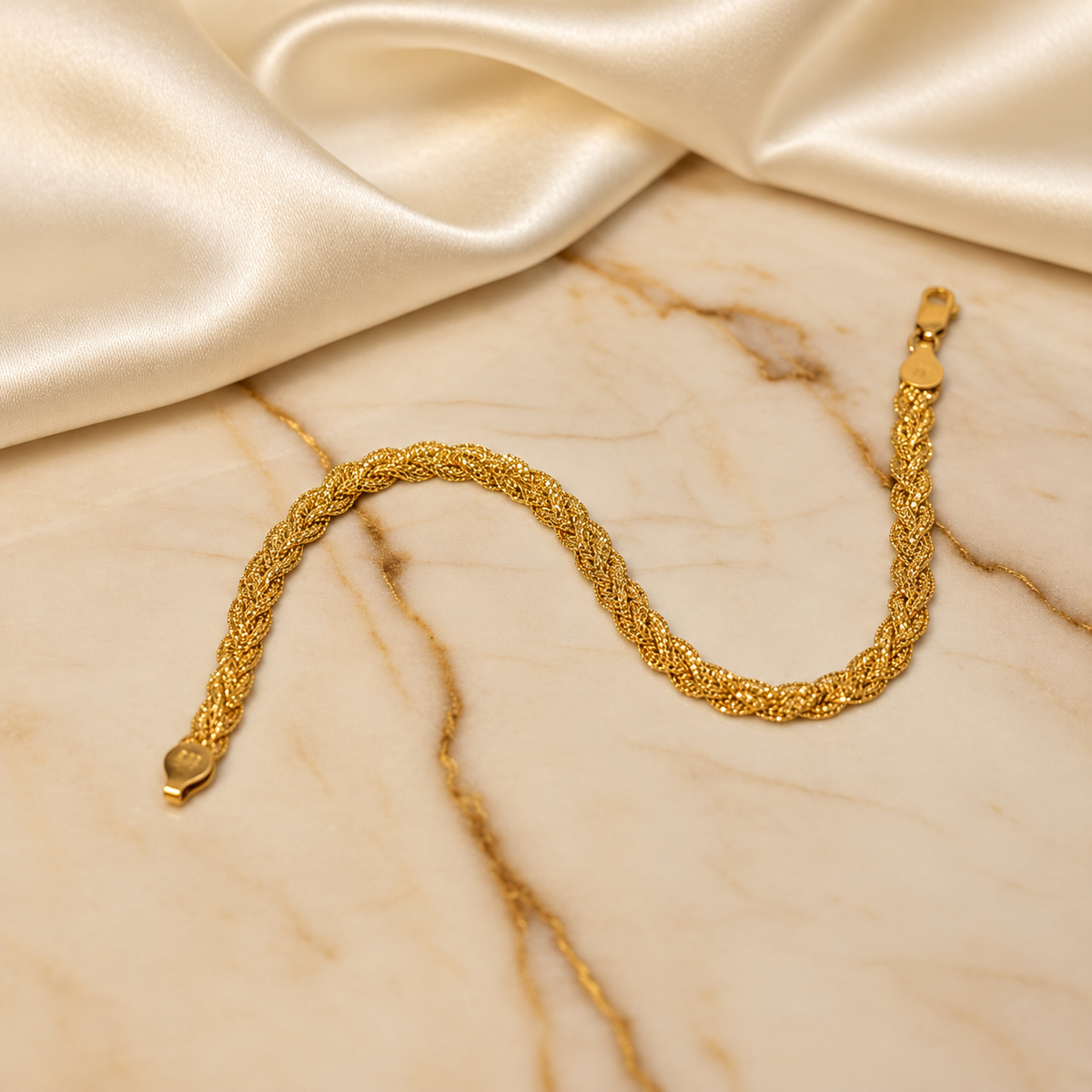 916 gold Wave Braided Bracelet arranged in a wave on cream marble beside satin