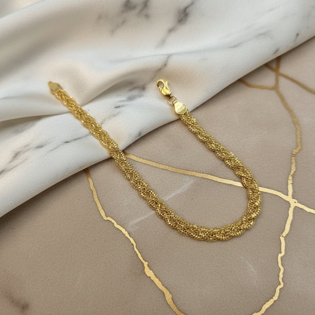 Guild Bullion 916 gold wave braided bracelet in a U shape on grey and marble-pattern fabric with lobster clasp visible