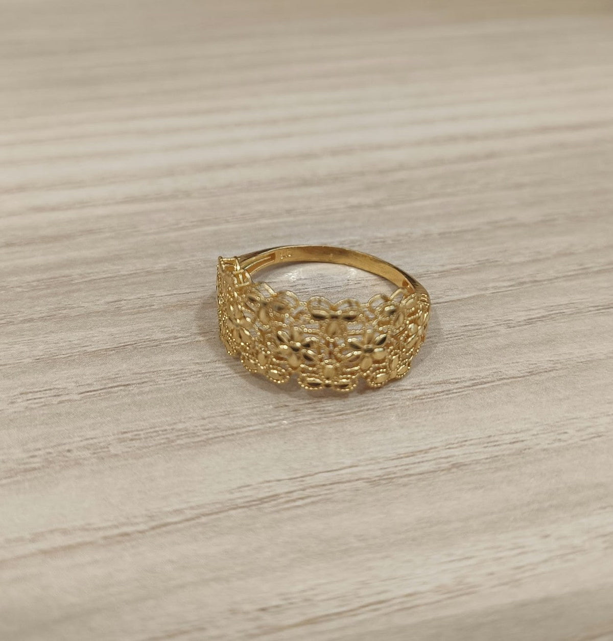 Guild Bullion 916 yellow gold Serenity Petal ring with openwork flowers and smooth back shank on light wood