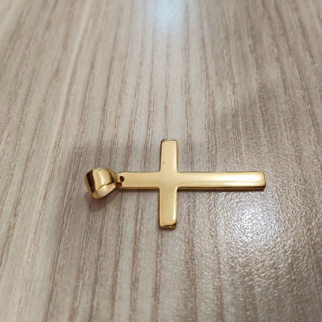 Polished 916 gold cross pendant lying sideways on a wood-grain surface