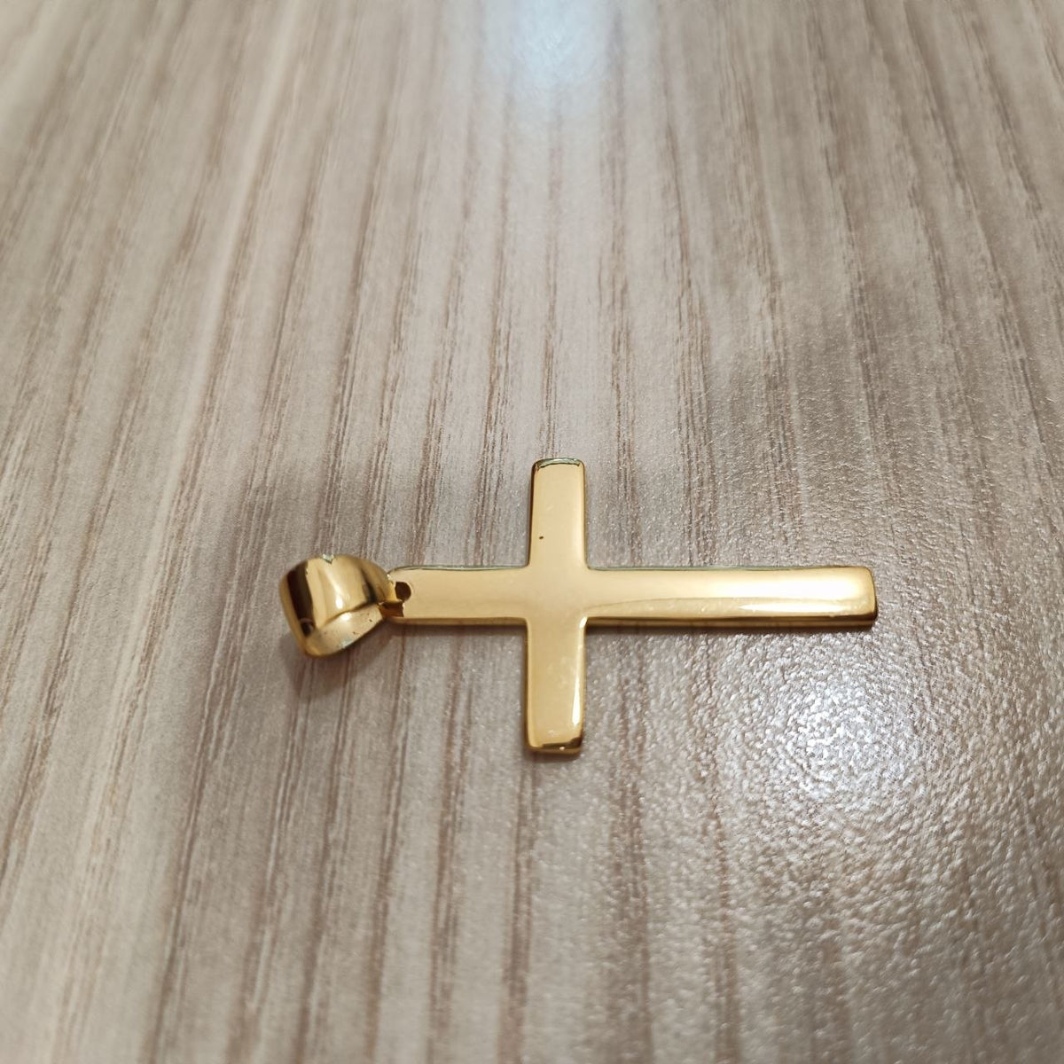 Polished 916 gold cross pendant lying sideways on a wood-grain surface